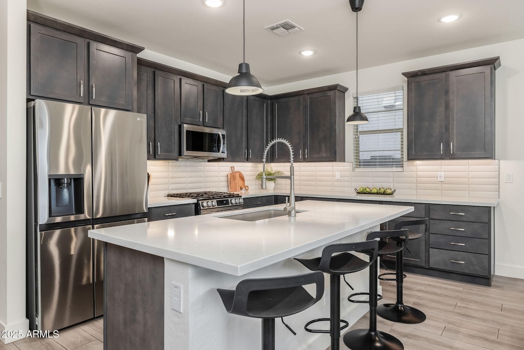 kitchen featuring sink, an island with sink, decorative light fixtures, dark brown cabinets, and stainless steel appliances