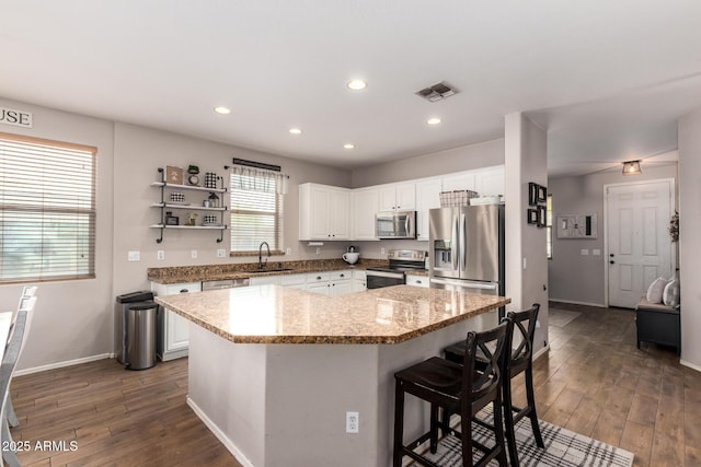 kitchen with appliances with stainless steel finishes, a center island, white cabinets, and light stone counters