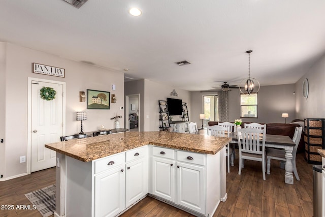 kitchen with pendant lighting, white cabinetry, a center island, light stone counters, and dark wood-type flooring