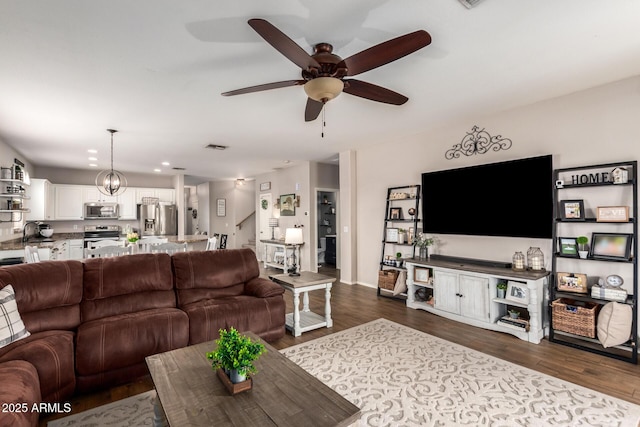 living room featuring dark wood-type flooring and ceiling fan with notable chandelier