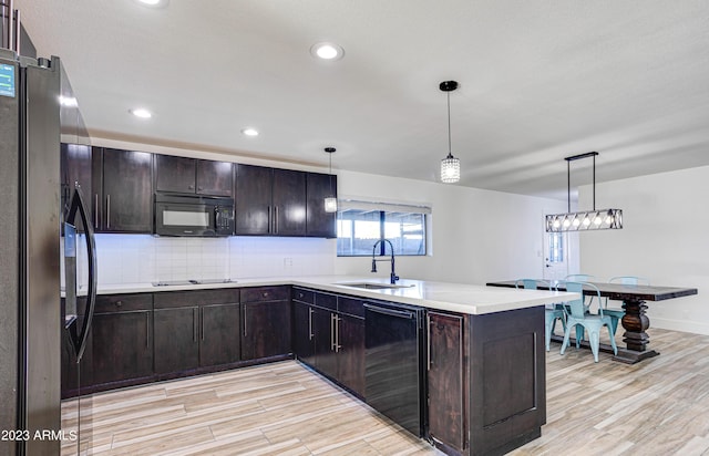 kitchen featuring a peninsula, black appliances, light wood-style flooring, and a sink