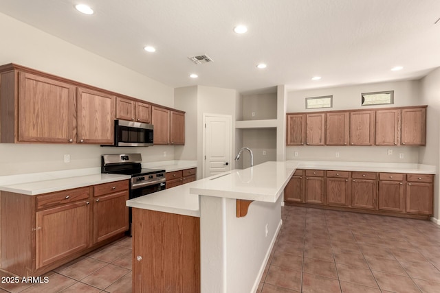 17419 W Elaine Dr, Goodyear, AZ 85338 - kitchen with appliances with stainless steel finishes, light tile patterned floors, brown cabinetry, recessed lighting, and a kitchen island with sink