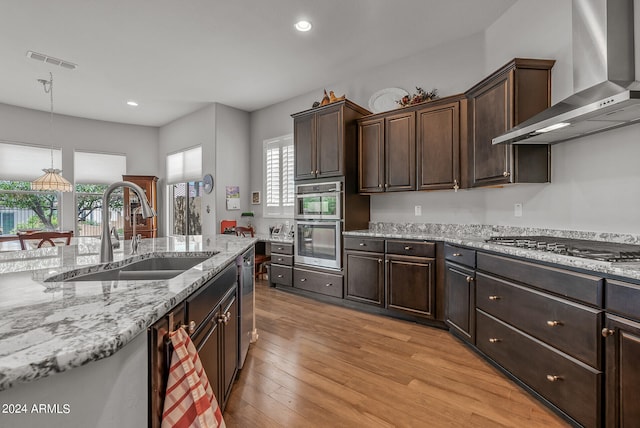 kitchen with dark brown cabinets, light wood-type flooring, wall chimney exhaust hood, and sink