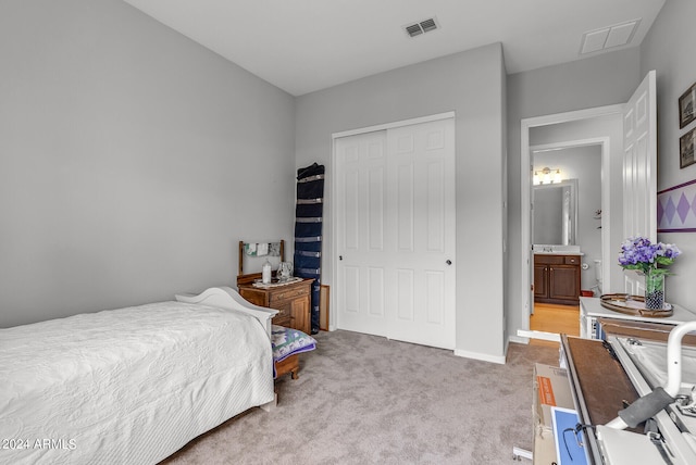 bedroom with light colored carpet, a closet, and ensuite bath