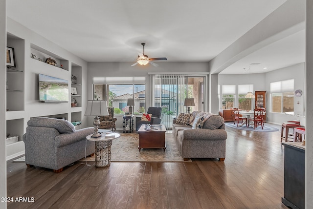 living room featuring built in shelves, dark hardwood / wood-style flooring, and ceiling fan