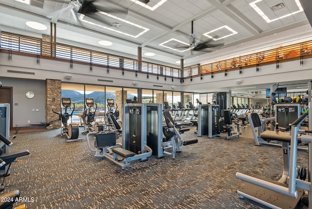 workout area featuring coffered ceiling, carpet, ceiling fan, and a high ceiling