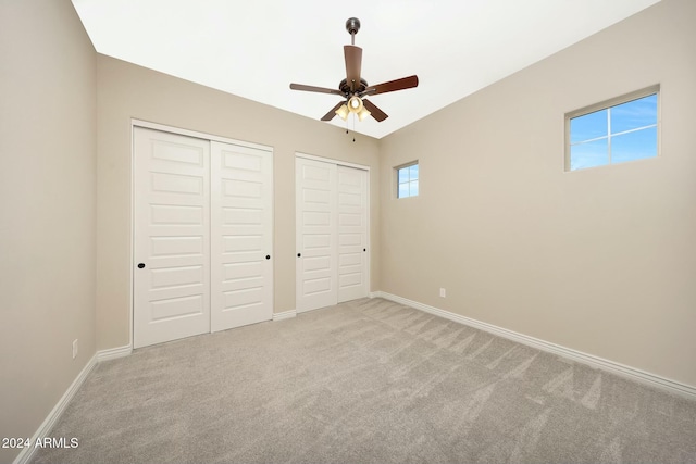 unfurnished bedroom featuring ceiling fan, light carpet, and multiple closets