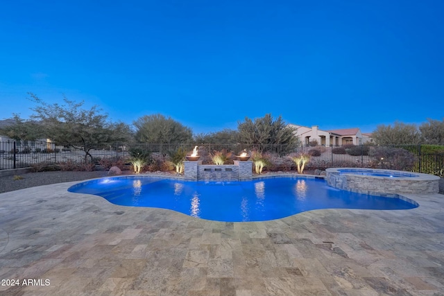 pool at dusk featuring an in ground hot tub, pool water feature, and a patio area