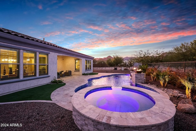 pool at dusk with an in ground hot tub and a patio