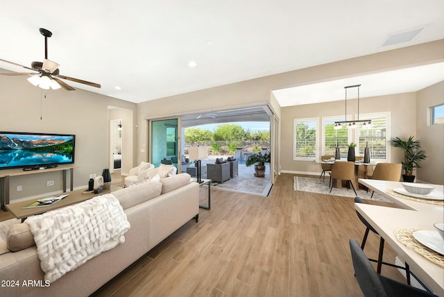 living room featuring ceiling fan with notable chandelier and light wood-type flooring