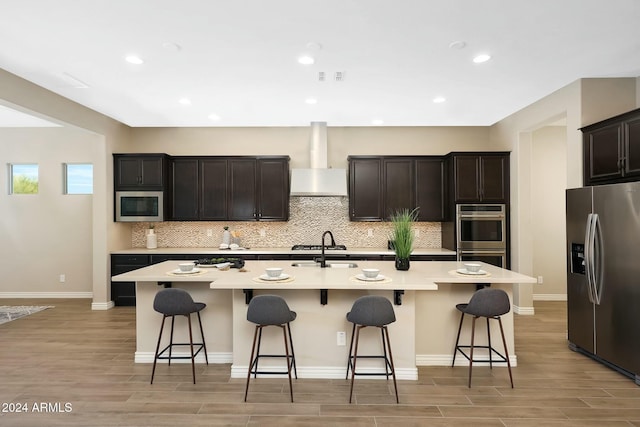 20594 W Pasadena Ave, Buckeye, AZ 85396 - kitchen featuring appliances with stainless steel finishes, wall chimney exhaust hood, tasteful backsplash, light wood-style floors, and recessed lighting