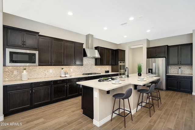 20594 W Pasadena Ave, Buckeye, AZ 85396 - kitchen with stainless steel appliances, wall chimney exhaust hood, decorative backsplash, light wood-style floors, and a kitchen bar