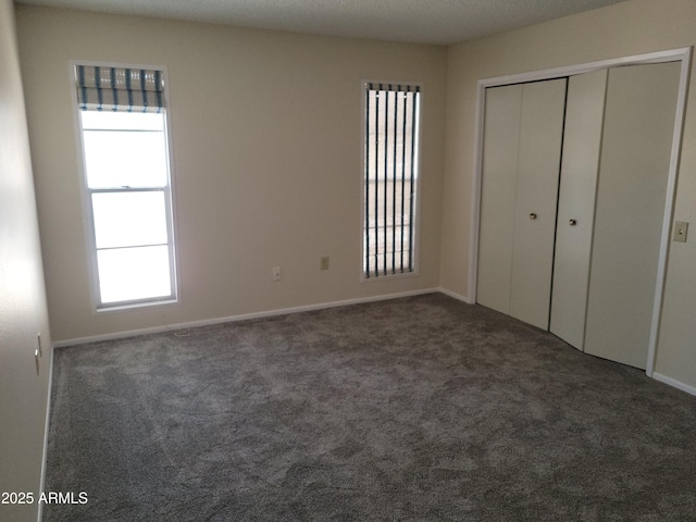 unfurnished bedroom with multiple windows, dark carpet, and a closet