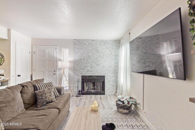 living room with a textured ceiling, hardwood / wood-style flooring, and a stone fireplace