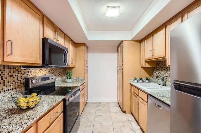 kitchen featuring sink, light stone countertops, appliances with stainless steel finishes, tasteful backsplash, and a tray ceiling