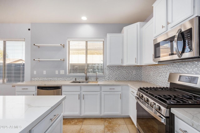 kitchen with tasteful backsplash, appliances with stainless steel finishes, white cabinetry, a sink, and light stone countertops