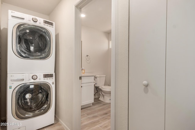 clothes washing area with baseboards, stacked washing maching and dryer, laundry area, and light wood finished floors