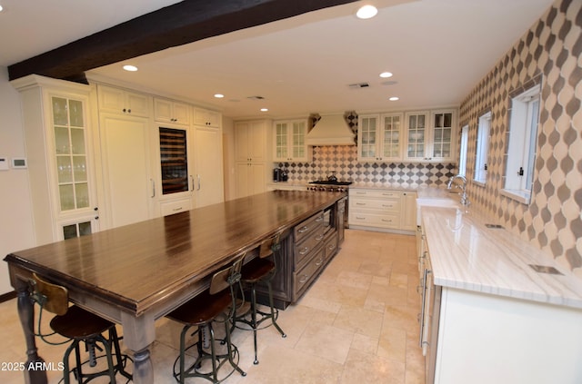 kitchen with decorative backsplash, premium range hood, sink, beam ceiling, and a center island