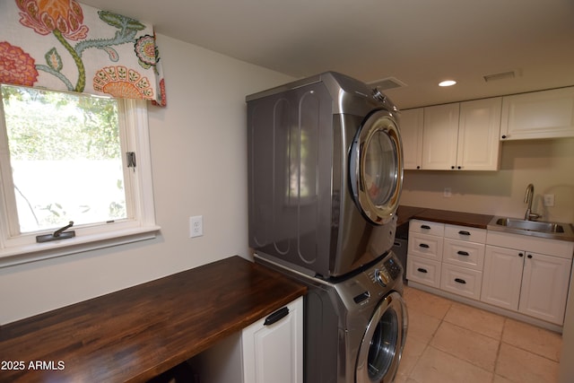 clothes washing area featuring stacked washer / dryer, sink, and light tile patterned floors