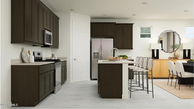 11946 W Calle De Pompas, Peoria, AZ 85383 - kitchen featuring appliances with stainless steel finishes, light wood-style floors, a kitchen island with sink, light countertops, and a kitchen breakfast bar