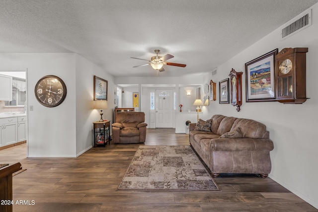 living room featuring ceiling fan, dark wood-type flooring, and a textured ceiling