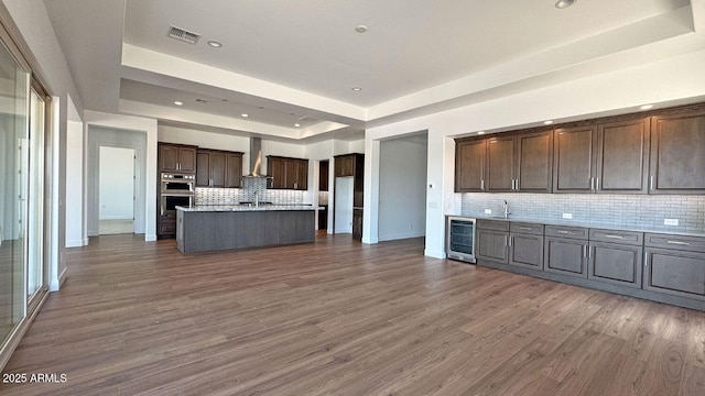 16777 W Sheila Ln, Goodyear, AZ 85395 - kitchen featuring a raised ceiling, wine cooler, backsplash, stainless steel double oven, and wall chimney exhaust hood