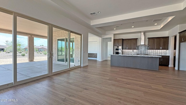 16777 W Sheila Ln, Goodyear, AZ 85395 - kitchen featuring a raised ceiling, wall chimney exhaust hood, decorative backsplash, dark brown cabinets, and stainless steel double oven