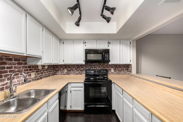 kitchen featuring dark wood-type flooring, a sink, decorative backsplash, black appliances, and a tray ceiling