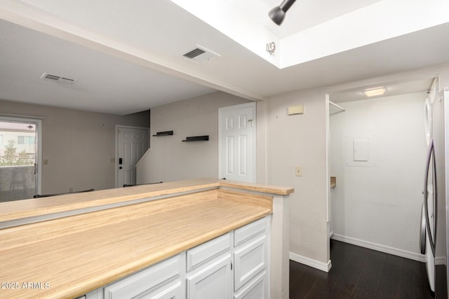 kitchen with dark wood-style floors, light countertops, freestanding refrigerator, white cabinets, and baseboards