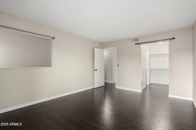 unfurnished bedroom featuring baseboards, a barn door, visible vents, and wood finished floors