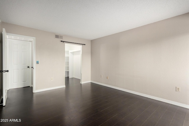 spare room with dark wood finished floors, visible vents, a barn door, a textured ceiling, and baseboards