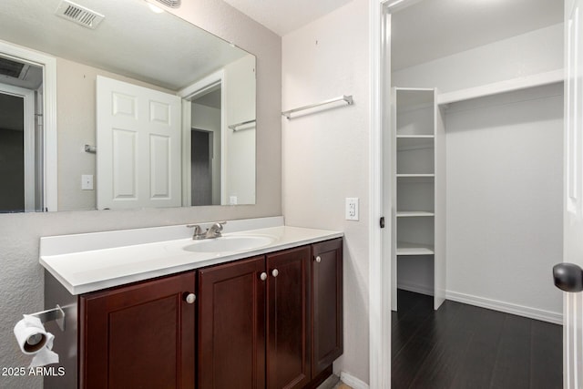 bathroom with visible vents, vanity, baseboards, and wood finished floors