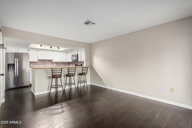 kitchen with dark wood finished floors, stainless steel refrigerator with ice dispenser, visible vents, black microwave, and a peninsula