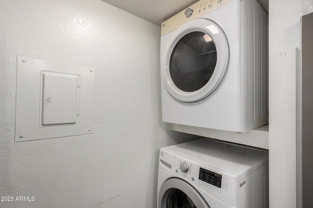 laundry area with stacked washer and dryer, laundry area, electric panel, and a textured wall