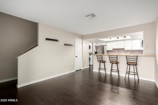 kitchen featuring dark wood-type flooring, visible vents, a kitchen breakfast bar, stacked washer / drying machine, and stainless steel fridge with ice dispenser