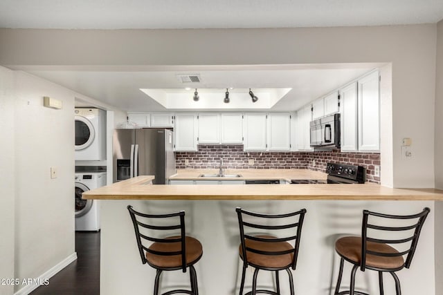 kitchen featuring visible vents, backsplash, stacked washer / dryer, a sink, and black appliances