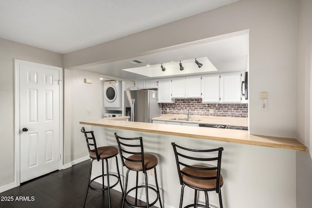 kitchen with stacked washer / dryer, a sink, light countertops, backsplash, and stainless steel fridge with ice dispenser