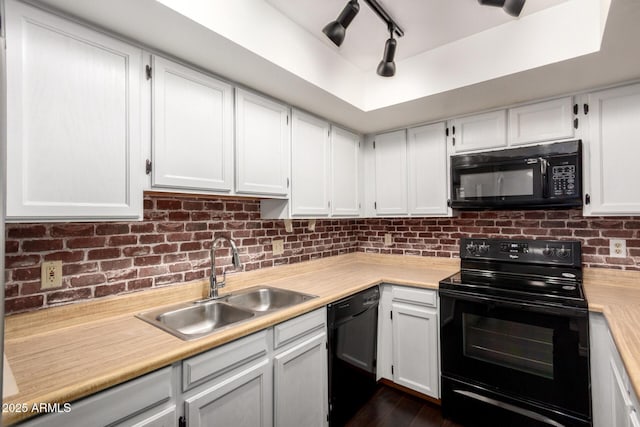 kitchen with a raised ceiling, light countertops, black appliances, white cabinetry, and a sink