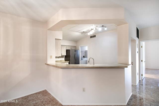 kitchen with visible vents, a sink, light countertops, freestanding refrigerator, and a peninsula