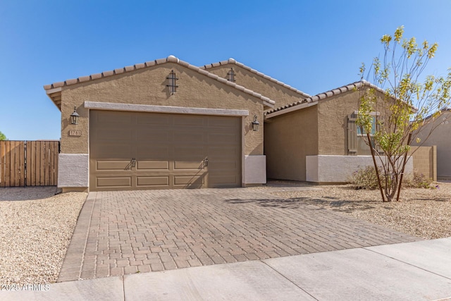 view of front facade with a garage, a tile roof, fence, decorative driveway, and stucco siding