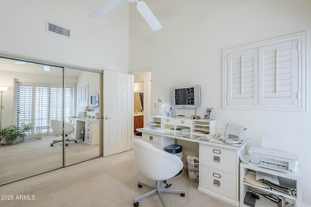 home office with visible vents, a towering ceiling, ceiling fan, and light colored carpet