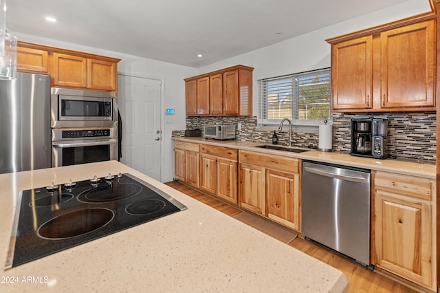 kitchen featuring sink, light stone counters, light hardwood / wood-style floors, decorative backsplash, and appliances with stainless steel finishes