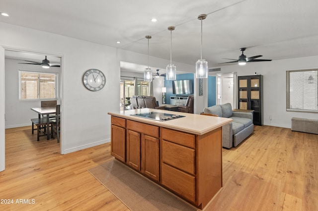 kitchen featuring light wood-type flooring, black electric stovetop, a center island, ceiling fan, and decorative light fixtures