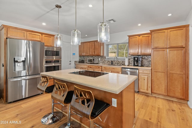 kitchen with appliances with stainless steel finishes, light hardwood / wood-style floors, a center island, pendant lighting, and sink