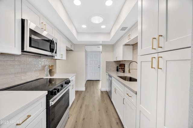 kitchen with white cabinetry, stainless steel appliances, light hardwood / wood-style flooring, sink, and decorative backsplash