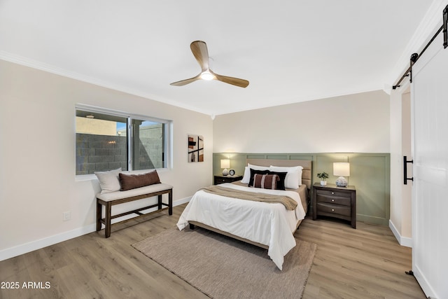 bedroom featuring ceiling fan, a barn door, crown molding, and light hardwood / wood-style flooring