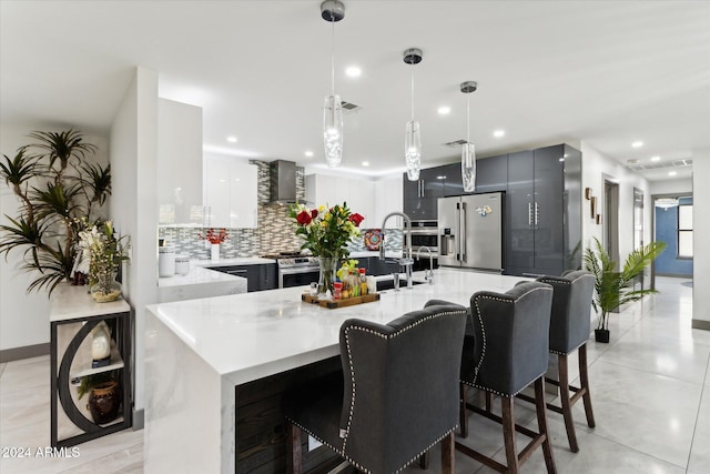 kitchen with wall chimney exhaust hood, tasteful backsplash, pendant lighting, a kitchen bar, and appliances with stainless steel finishes