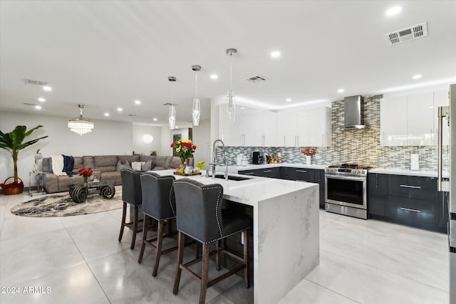 kitchen with wall chimney exhaust hood, stainless steel range oven, white cabinetry, and an island with sink