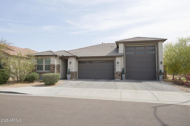 prairie-style home with an attached garage, driveway, stone siding, and stucco siding