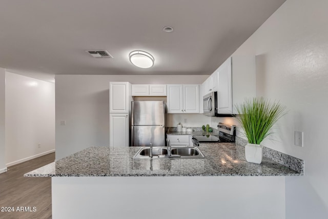 kitchen with kitchen peninsula, appliances with stainless steel finishes, sink, stone countertops, and white cabinets